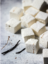 Load image into Gallery viewer, Tabletop with 12 white puffy square marshmallows dusted with powdered sugar, and drizzled with vanilla, decorated with two whole vanilla beans..
